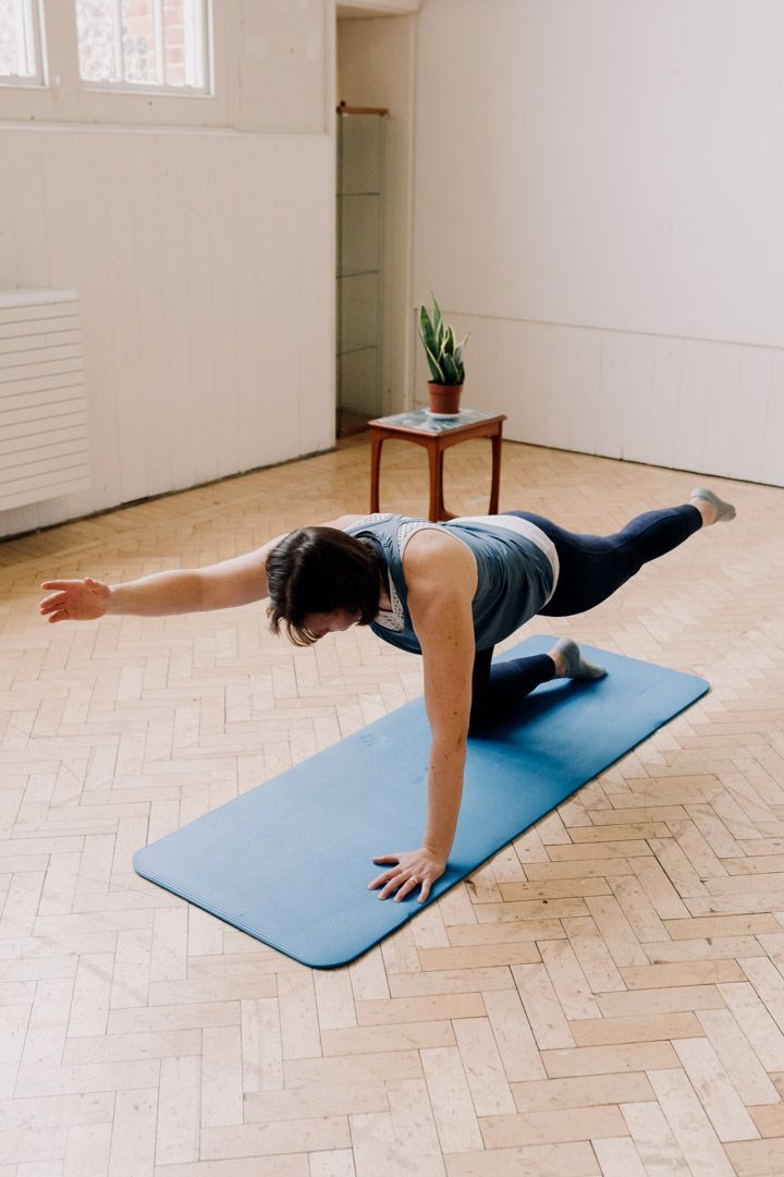 photo of a lady 4 point kneeling, raising an arm and leg into the air.