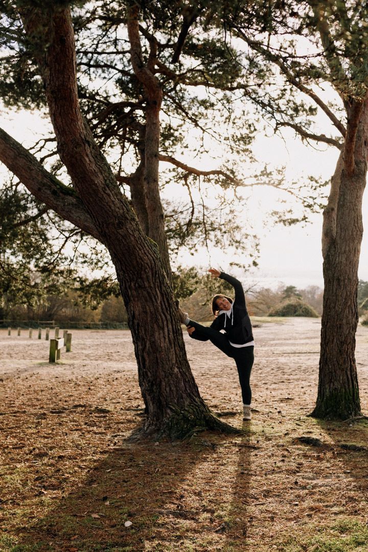 photo of a lady with her leg stretched up against a tree