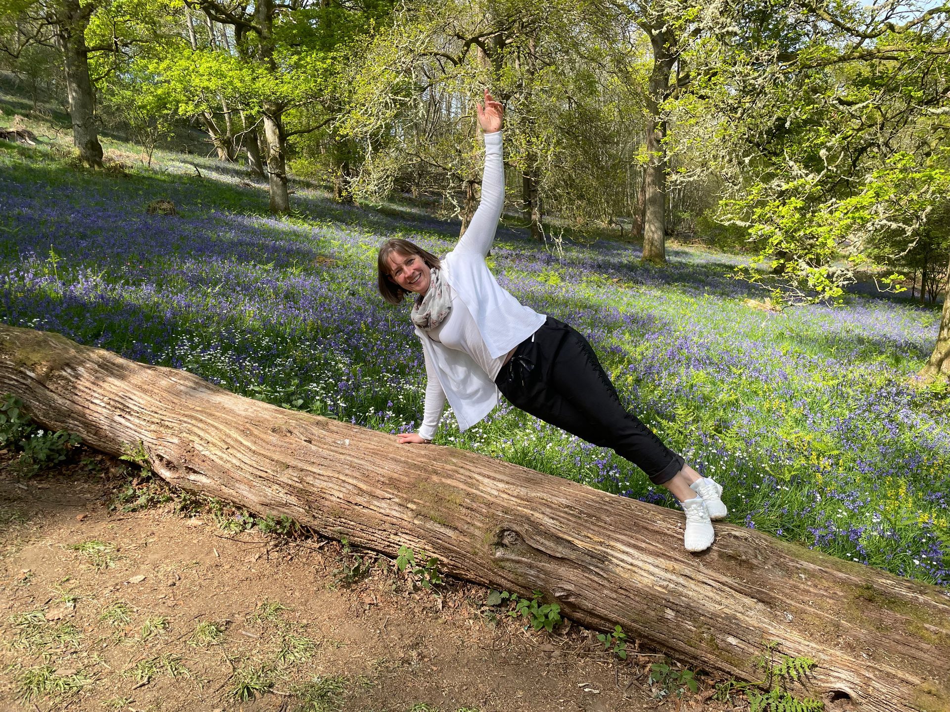 photo of instructor doing a Pilates side plank, on a fallen tree with bluebells covering the ground behind