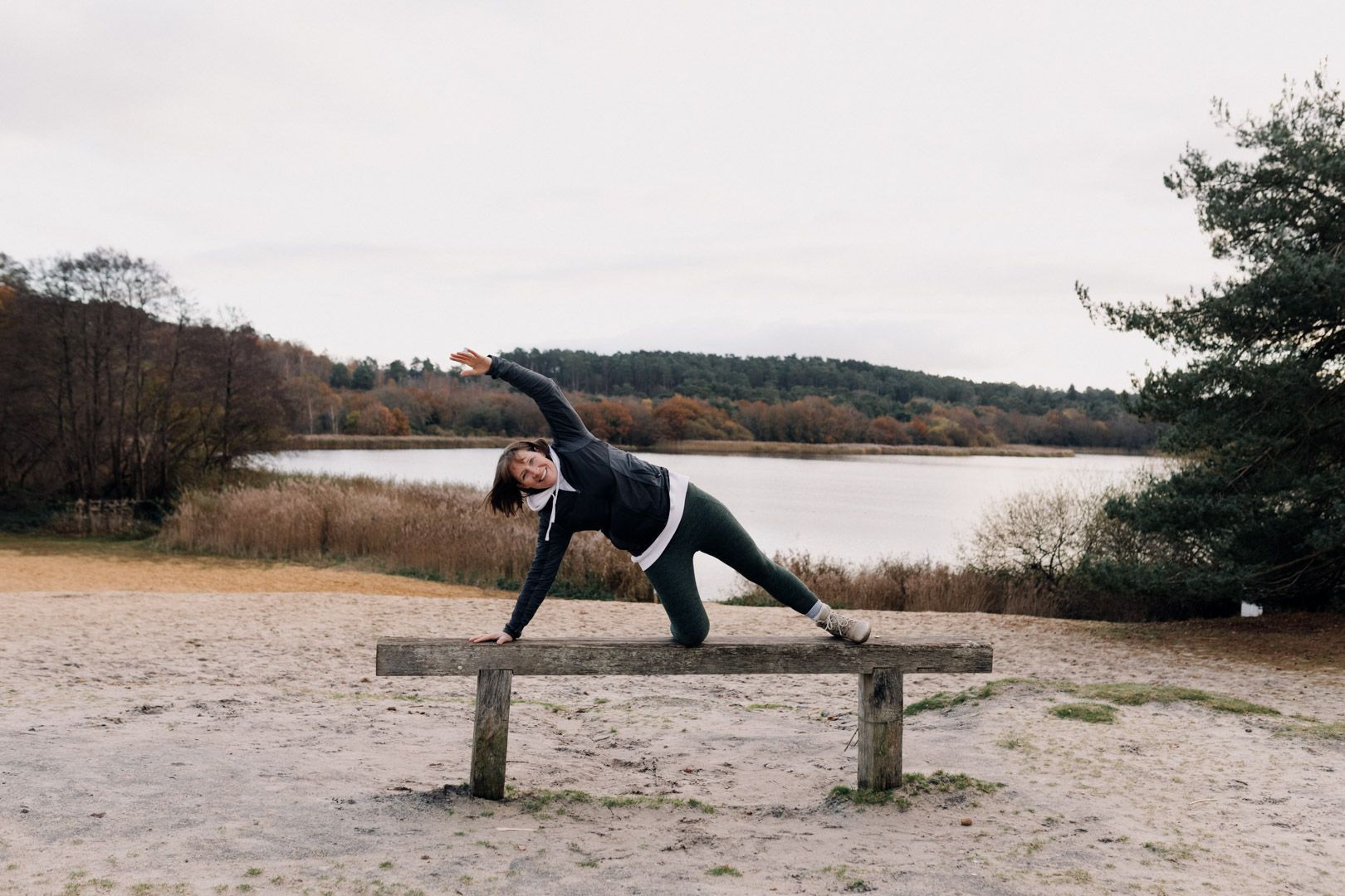 photo of a lady on a bench doing a side stretch with a lake and trees behind