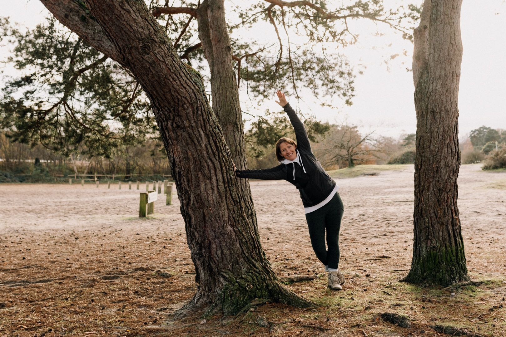 photo of a lady leaning on a tree, reaching an arm upwards