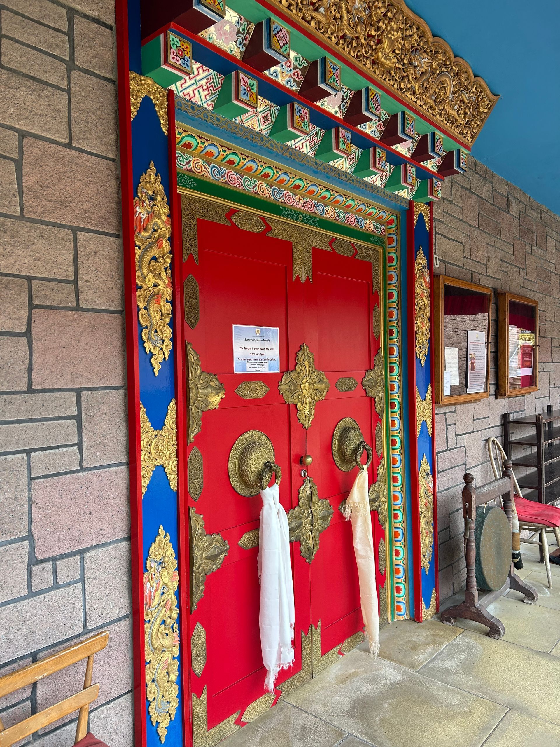 photo of a bright red temple door decorated with bright coloured and gold edging and scarves hanging from the handles