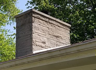 A chimney on the roof of a house with trees in the background