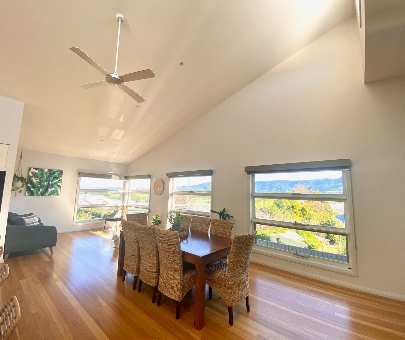 Bright dining room with wood floors, wicker chairs, and large windows overlooking a scenic landscape