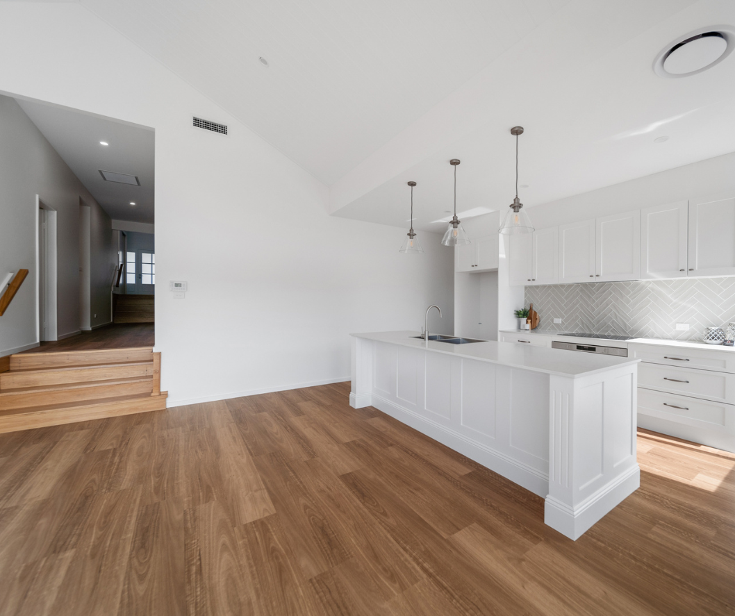 Bright modern kitchen with white cabinets, wood floors, island, and adjacent staircase hallway