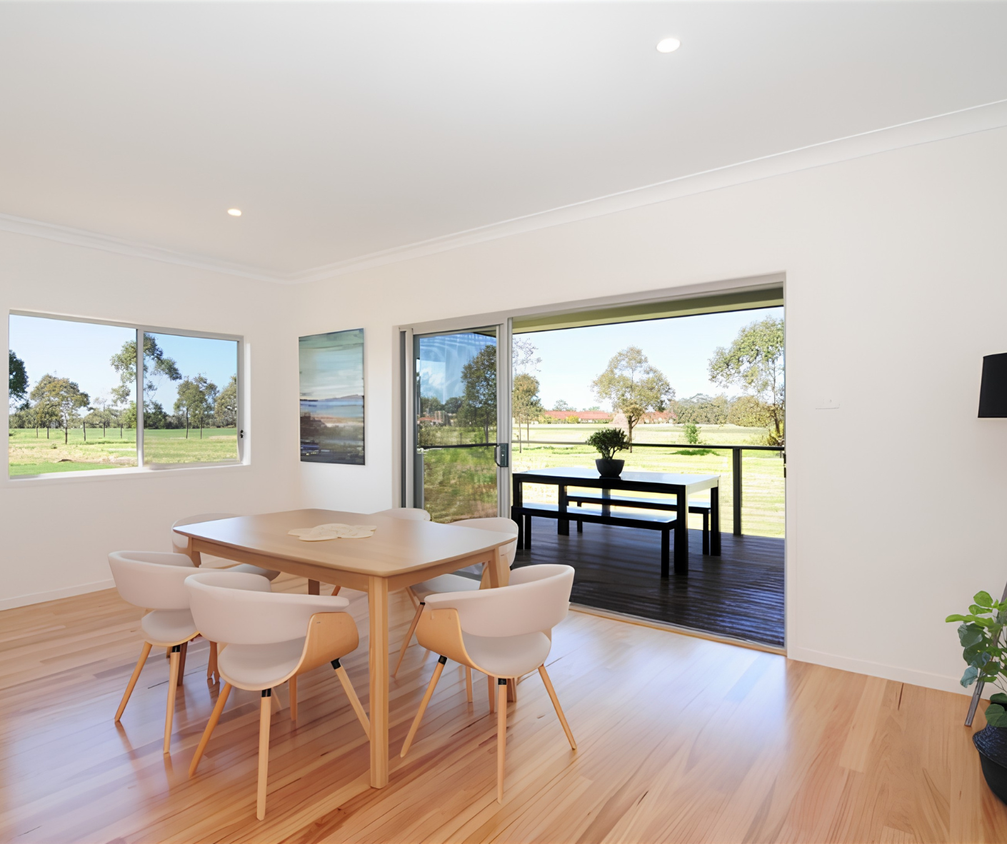 Bright dining room with wooden table, chairs, and large windows overlooking a grassy backyard.