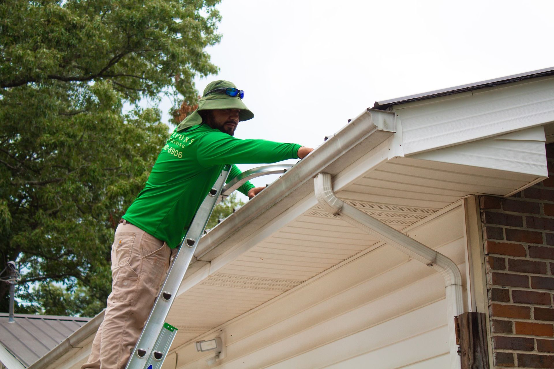 A man is standing on a ladder fixing a gutter on a house.