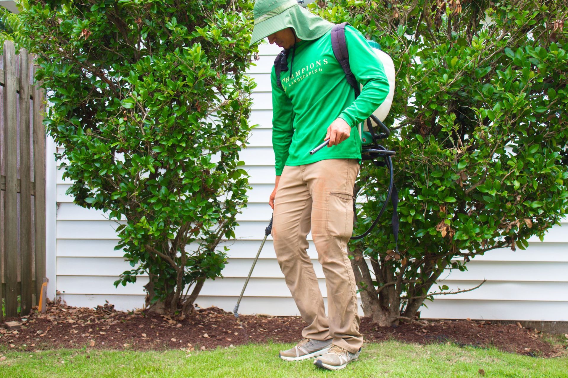 A man in a green shirt is spraying a lawn with a sprayer