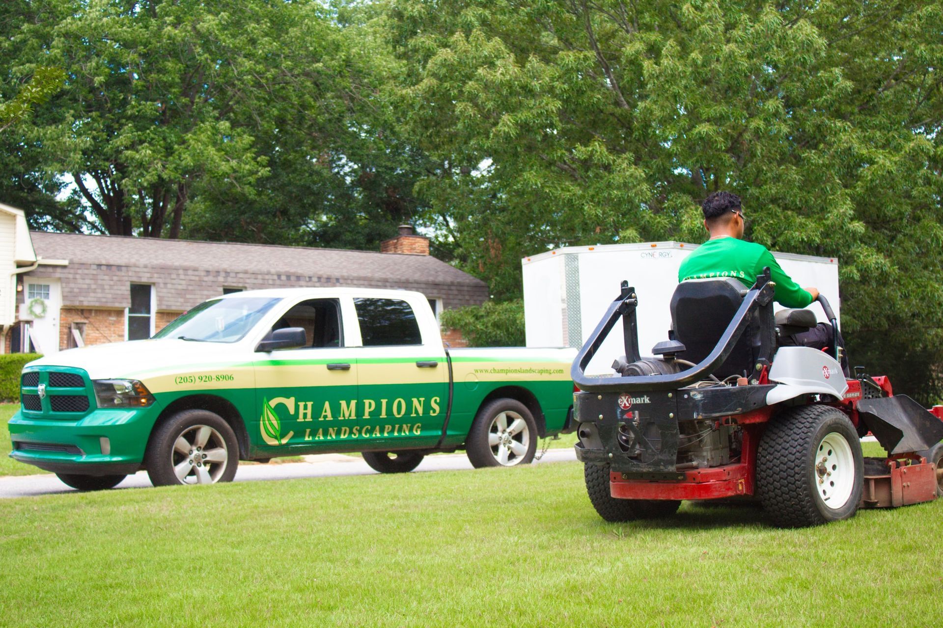 A man is riding a lawn mower next to a champions truck.