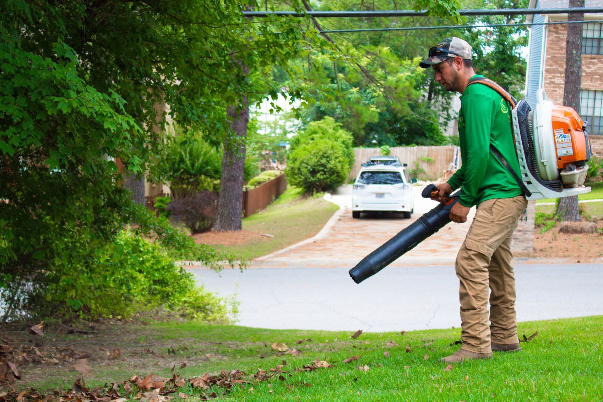 A man is blowing leaves from a lawn with a backpack blower.