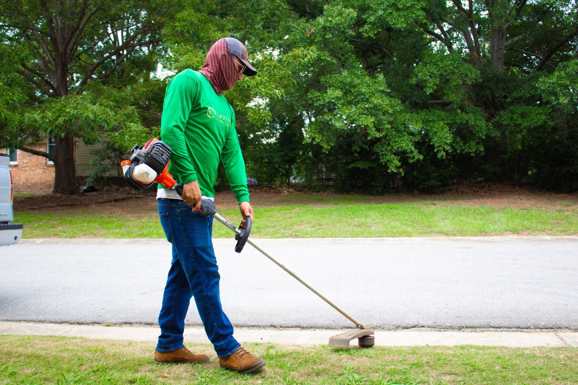 A man in a green shirt is using a weed eater to cut the grass.