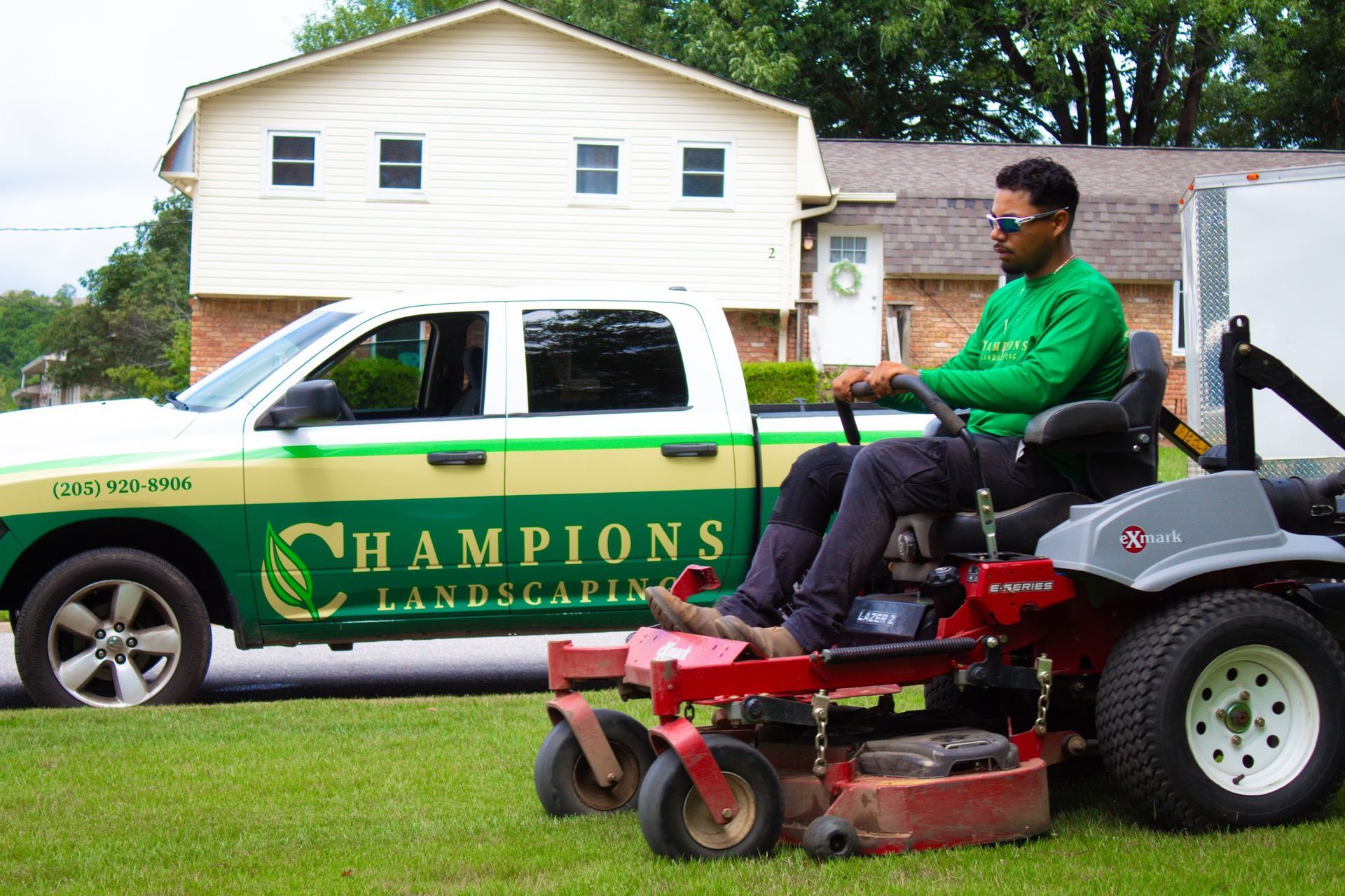 A man is riding a lawn mower in front of a champions truck.