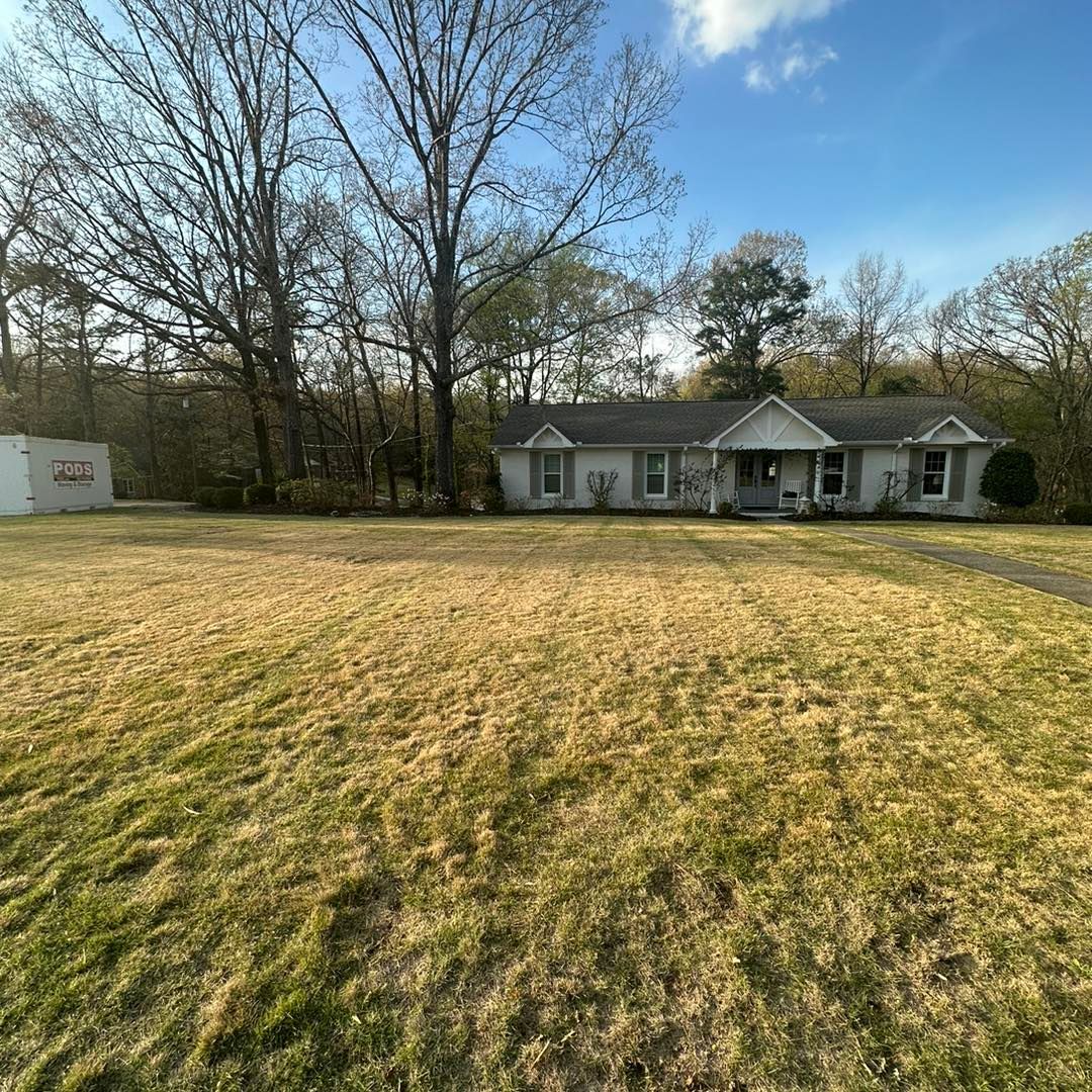A large house is sitting on top of a lush green field surrounded by trees.