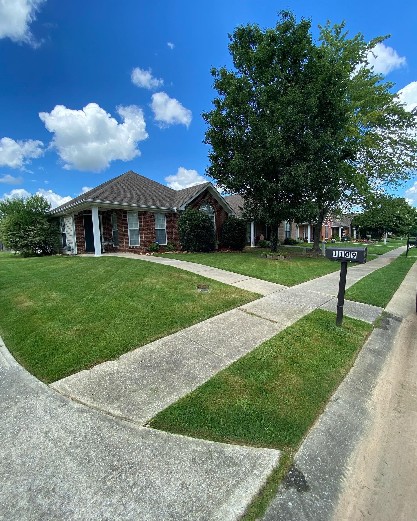 A brick house with a lush green lawn and a mailbox in front of it.