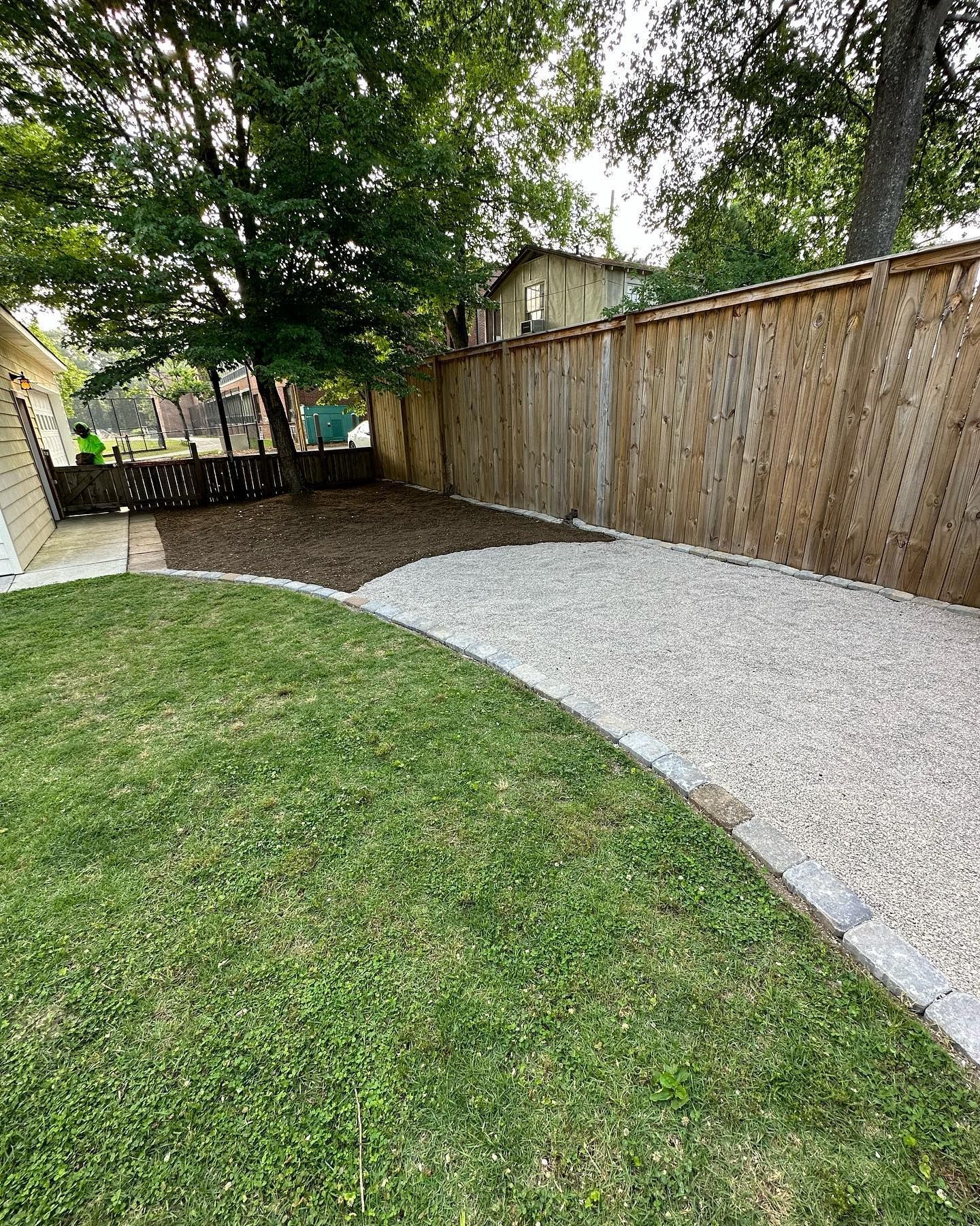 A backyard with a wooden fence and a gravel walkway.