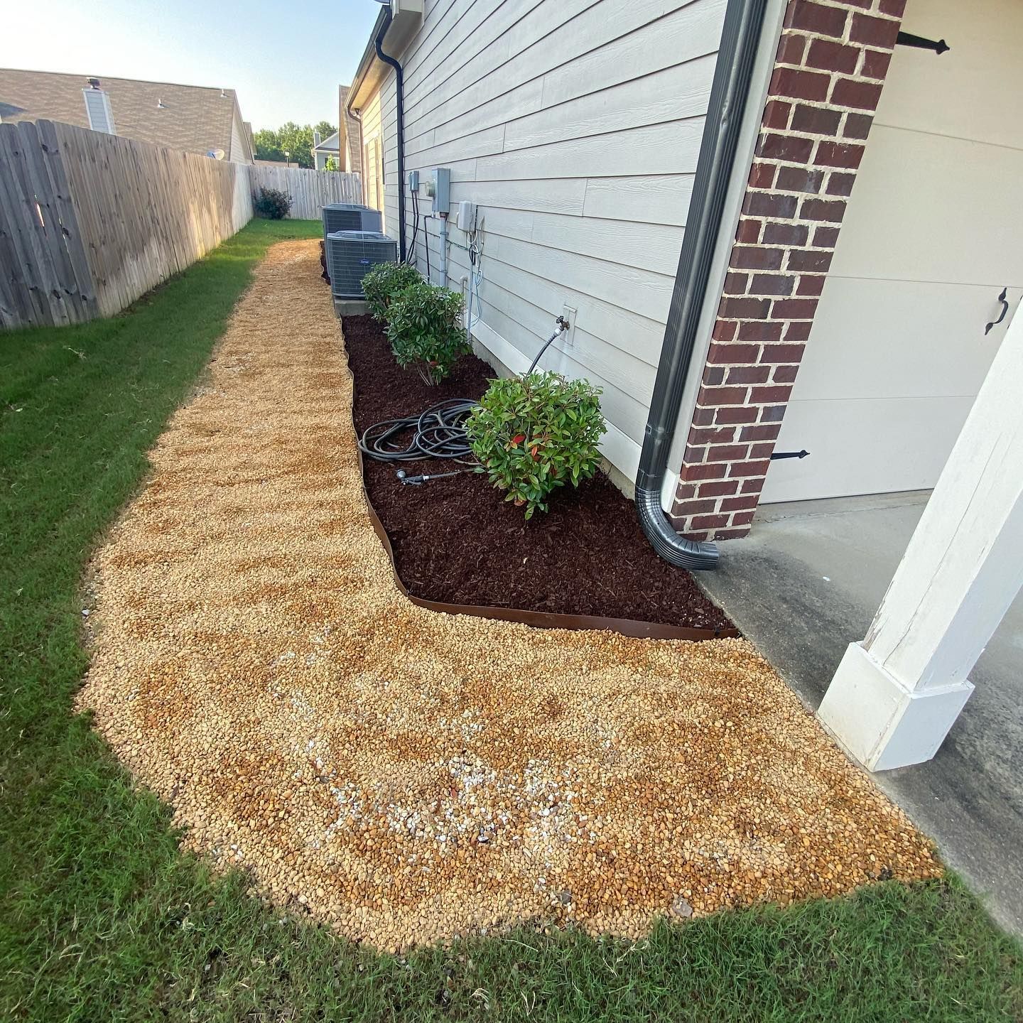 A sidewalk with mulch and plants in front of a house.