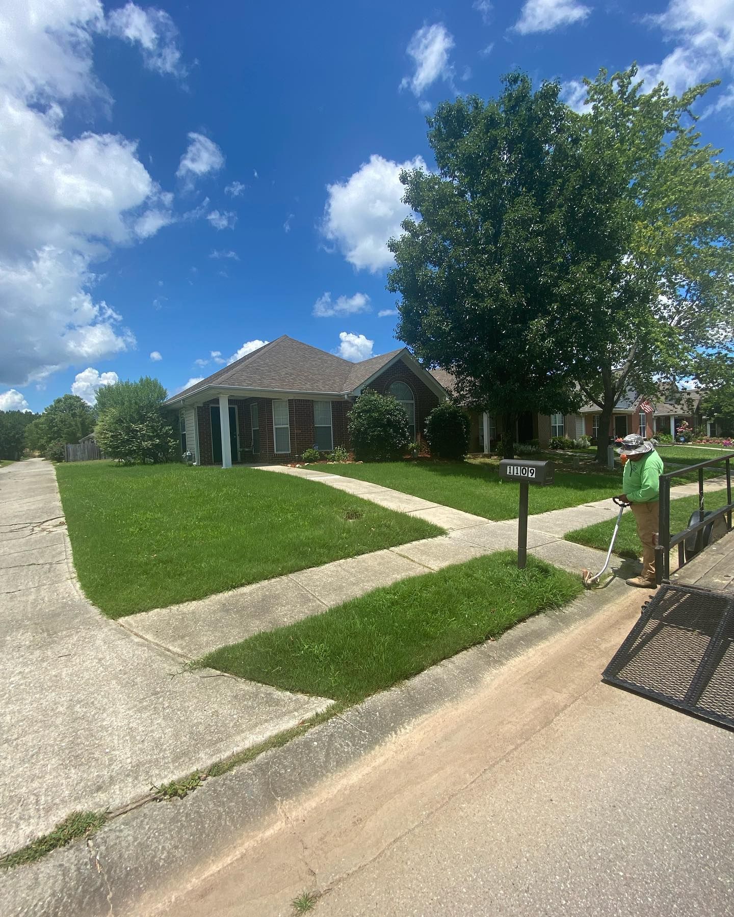 A man is mowing the grass in front of a house on a sunny day.