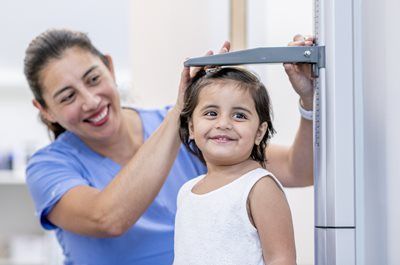 A healthcare worker measures a child's height with a stadiometer in a doctor's office.