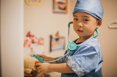 Young child in a surgeon's costume, examining a stuffed animal with a stethoscope.