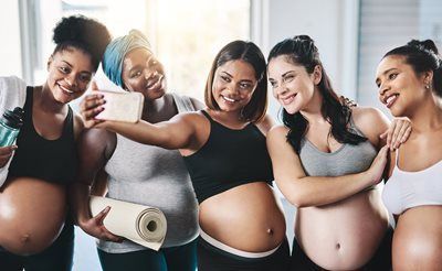 Five pregnant women smiling, taking a selfie together.