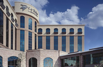 Sky Ridge Medical Center building exterior, beige with blue windows, under a blue sky.