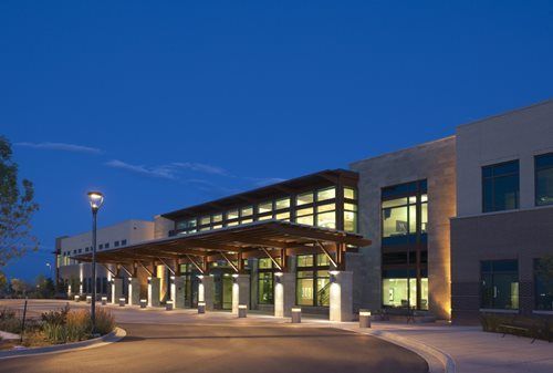 Modern building exterior at dusk, with illuminated entrance canopy and landscaping.