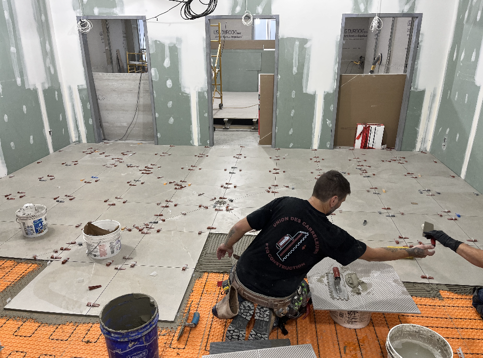 Un homme pose des carreaux sur le sol d'une pièce.
