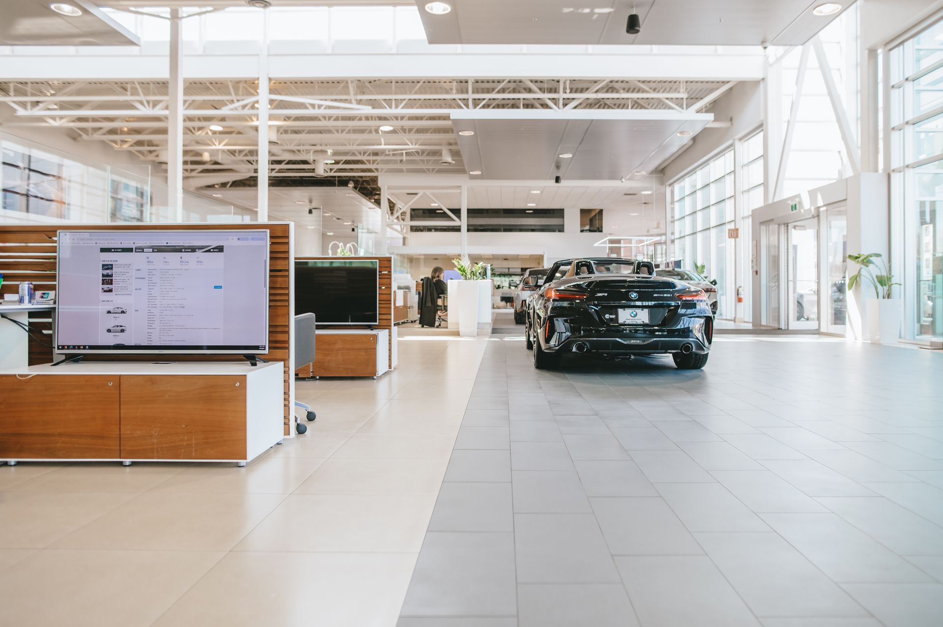 Une voiture est garée dans une salle d'exposition à côté d'une télévision.