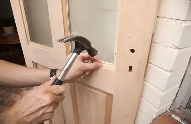 Hands use a hammer to nail a wood door panel into place.