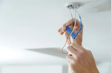 Hands installing exposed electrical wires in a ceiling light fixture