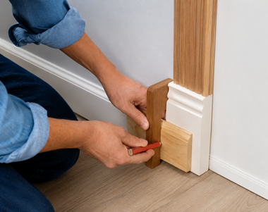 Hands installing wood trim around a door frame with a red pencil and sanding block.