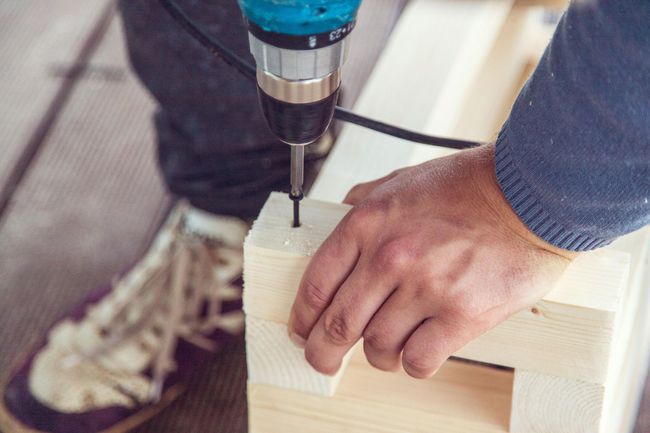 Hand drilling a hole in a light wood block with a blue power drill
