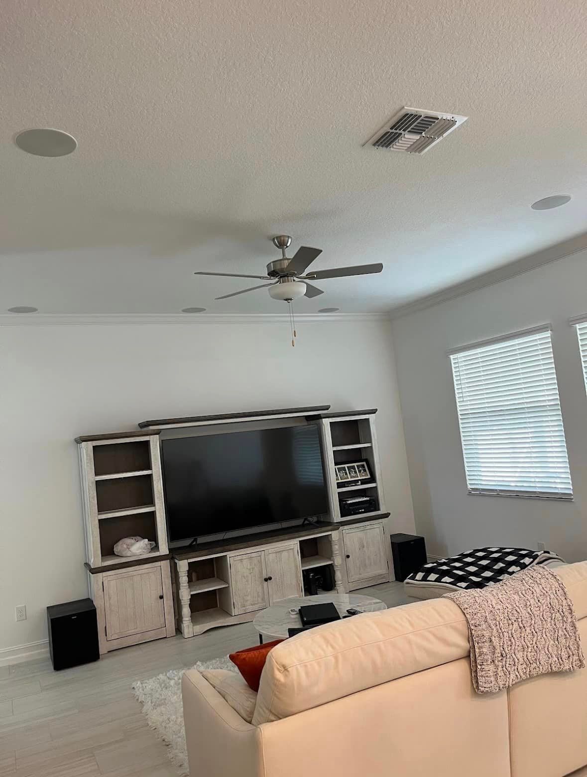 A living room with a couch , television , entertainment center and ceiling fan.