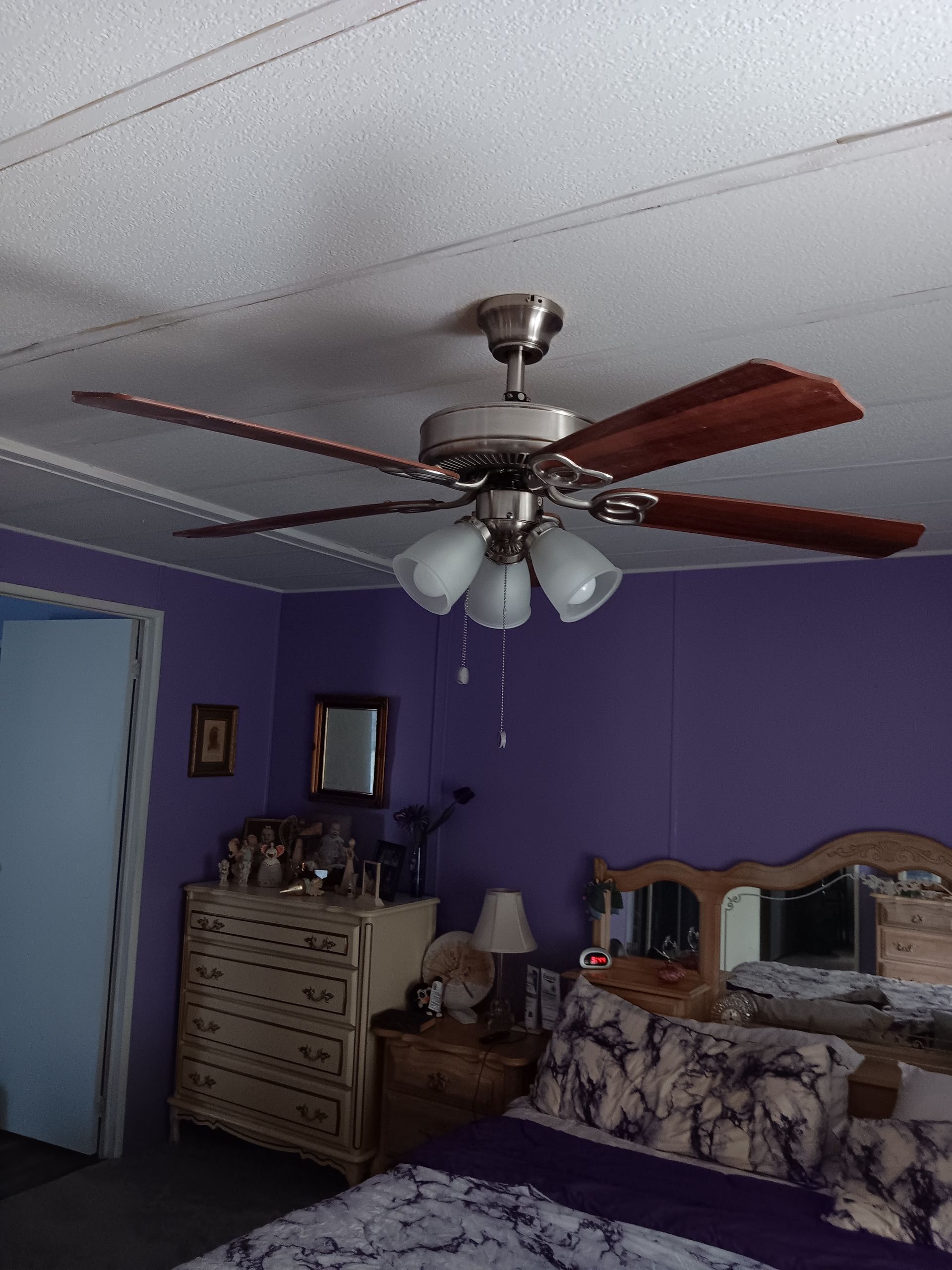 A bedroom with purple walls and a ceiling fan