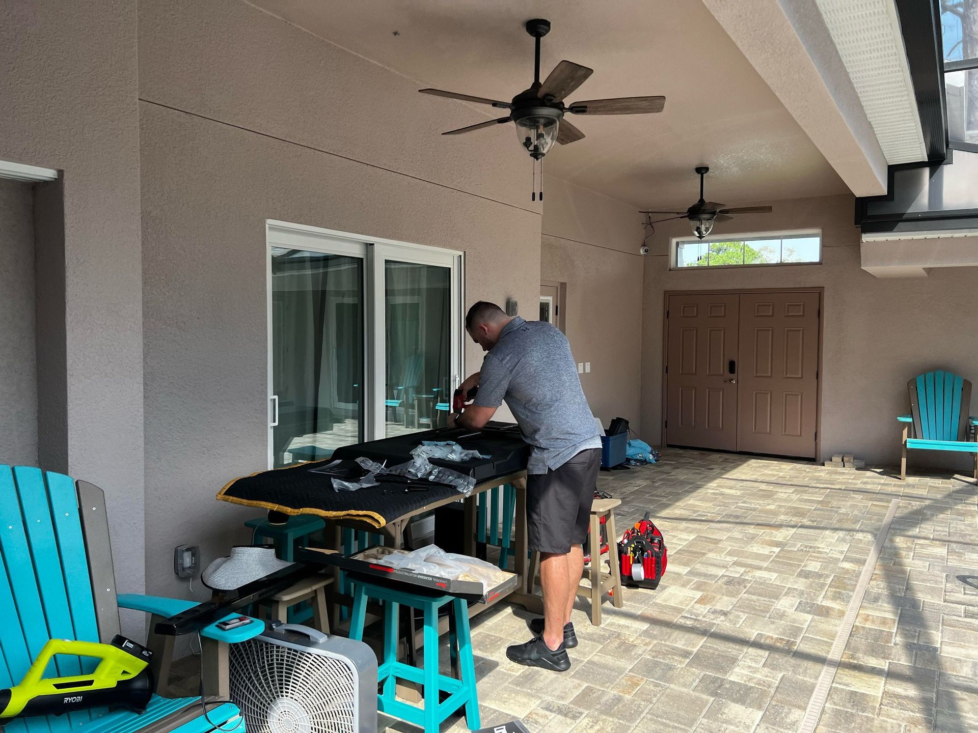 A man is working on a table on a patio with a ceiling fan.