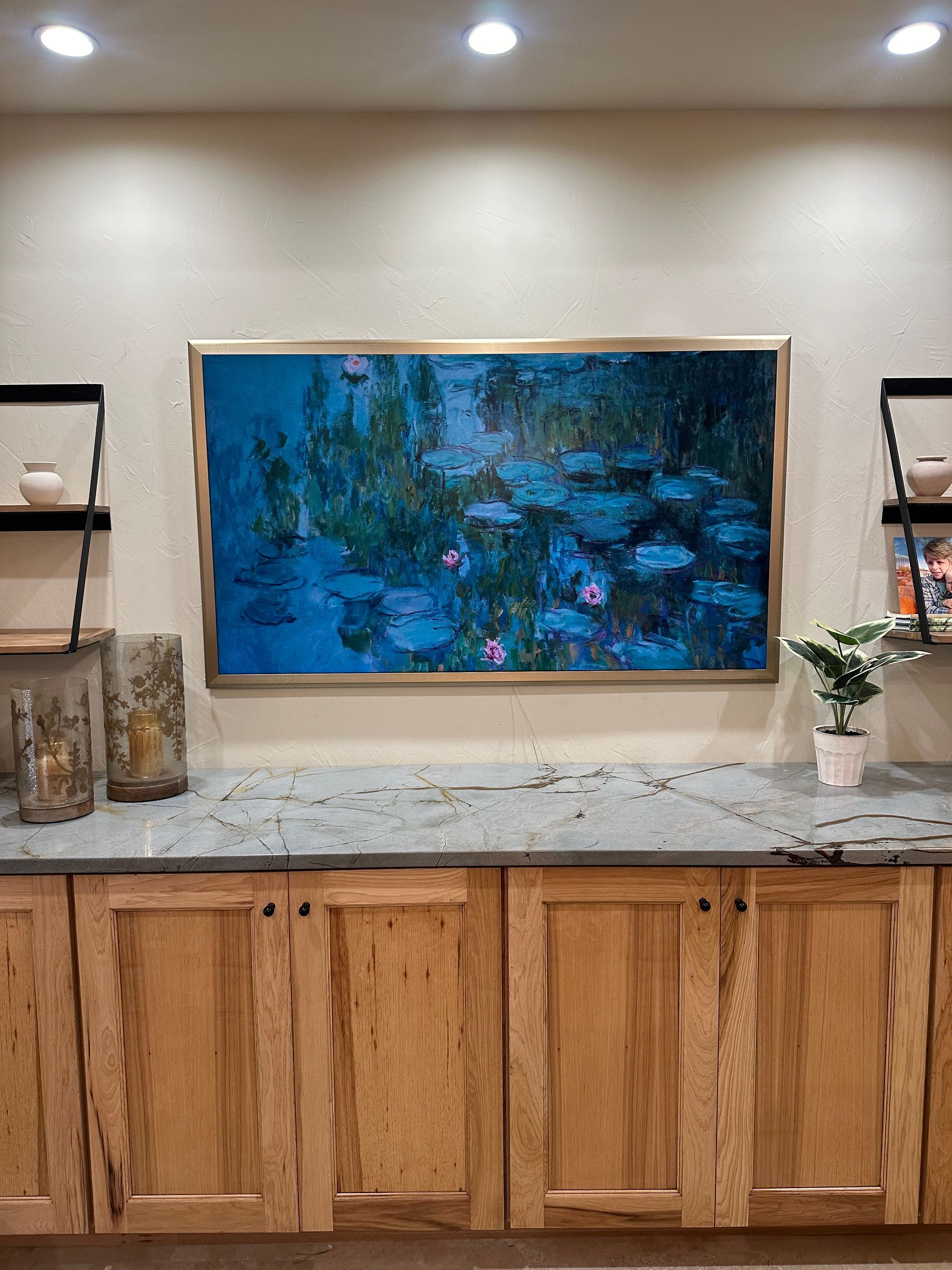 A large painting is hanging on the wall above a counter in a kitchen.