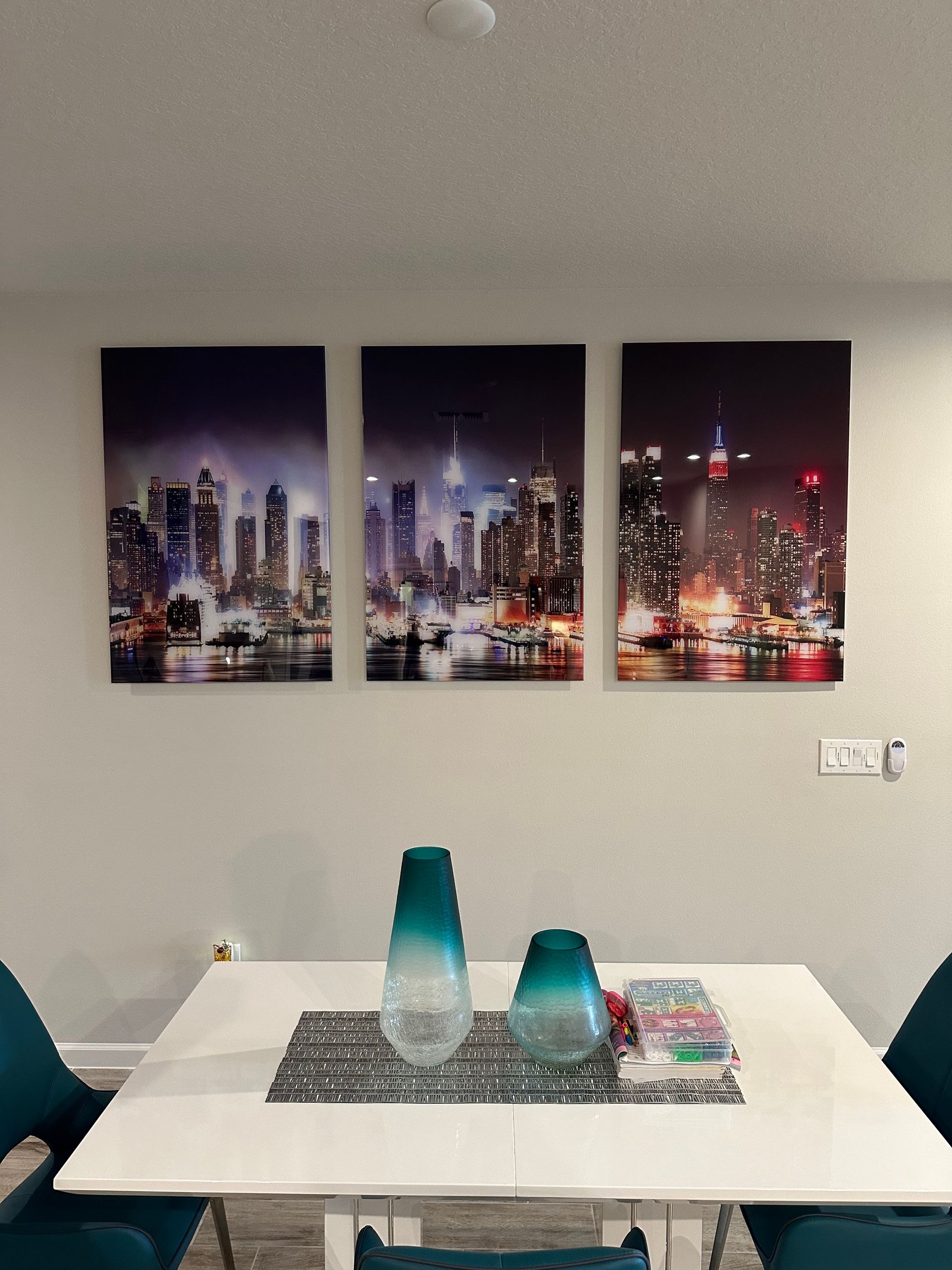 A dining room with a table and chairs and three paintings on the wall.