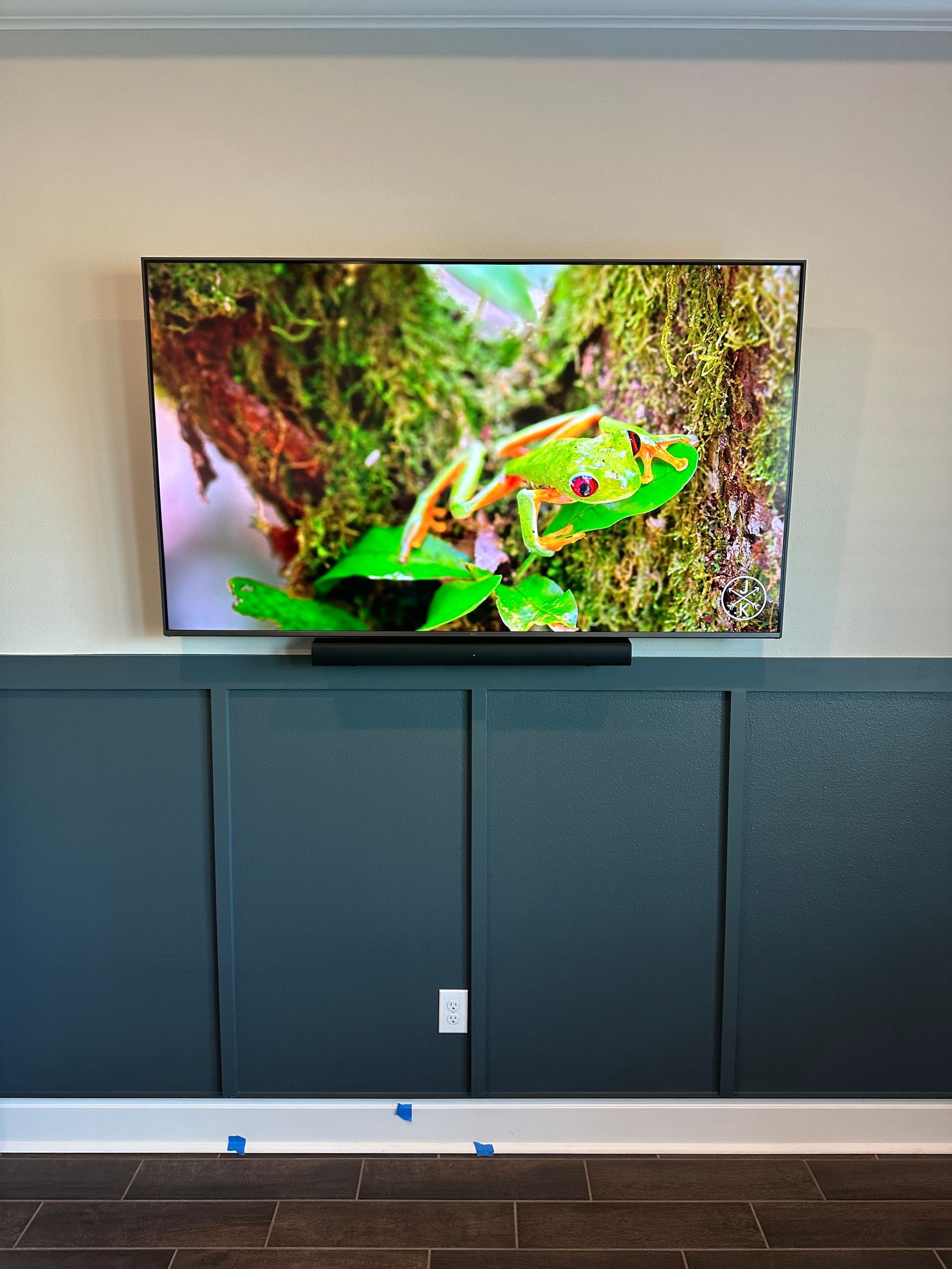 A television is hanging on a wall with a picture of a frog on it.