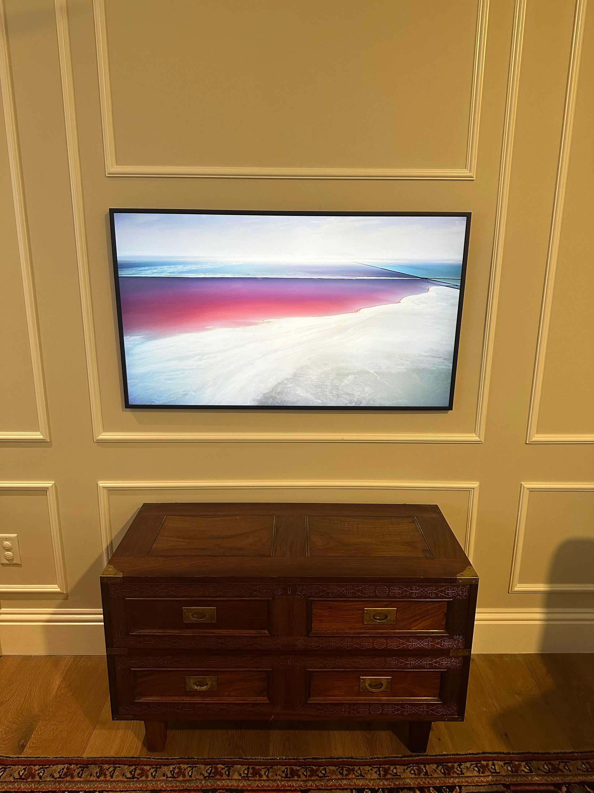 A flat screen tv is mounted on a wall above a wooden dresser.