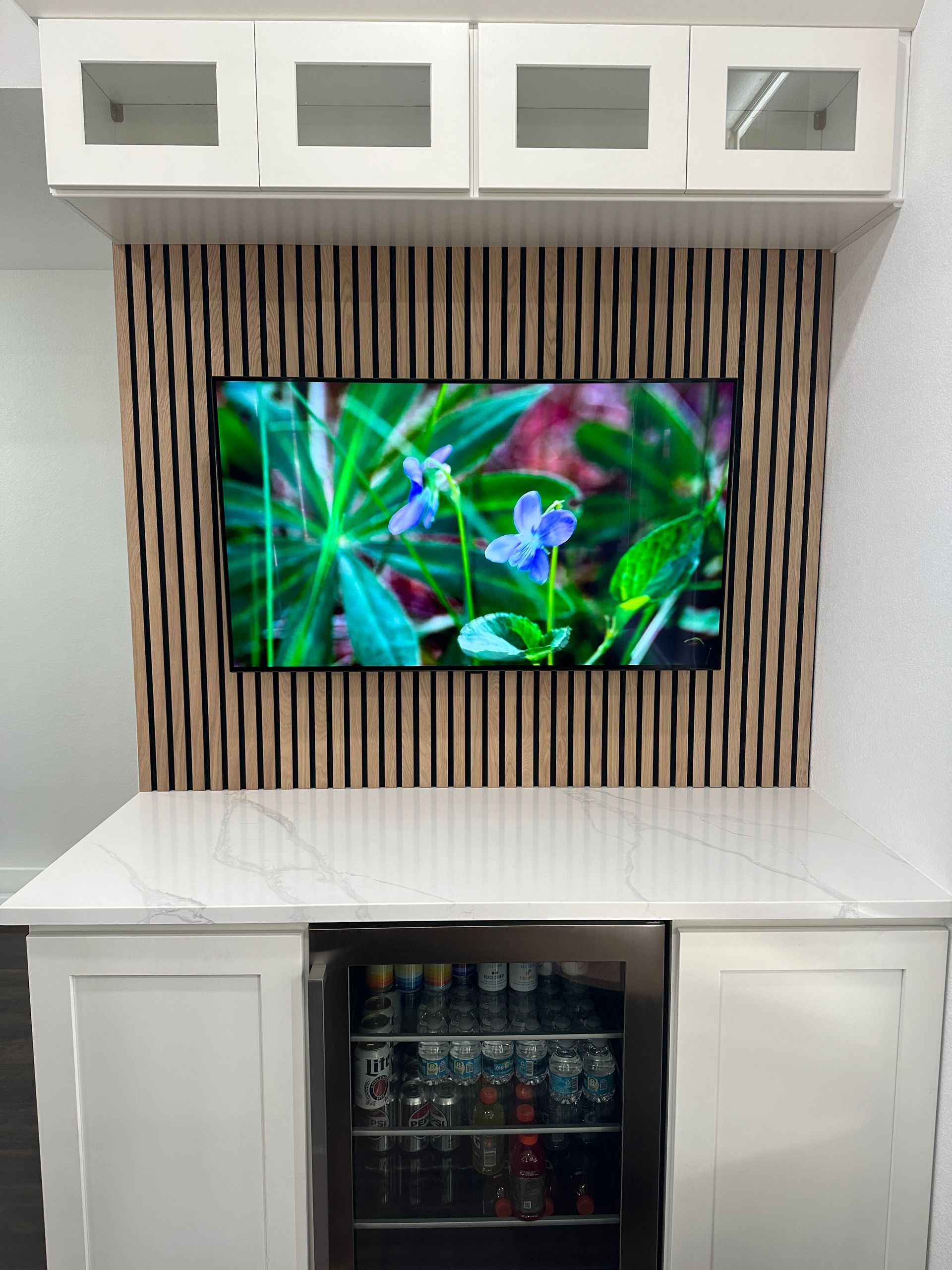 A kitchen with a refrigerator and a flat screen tv on the wall.