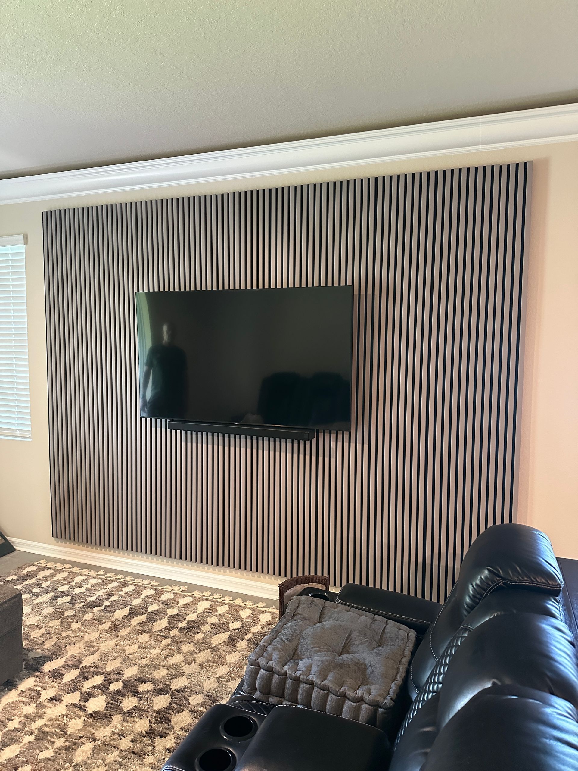 A living room with a striped wall and a flat screen tv on the wall.