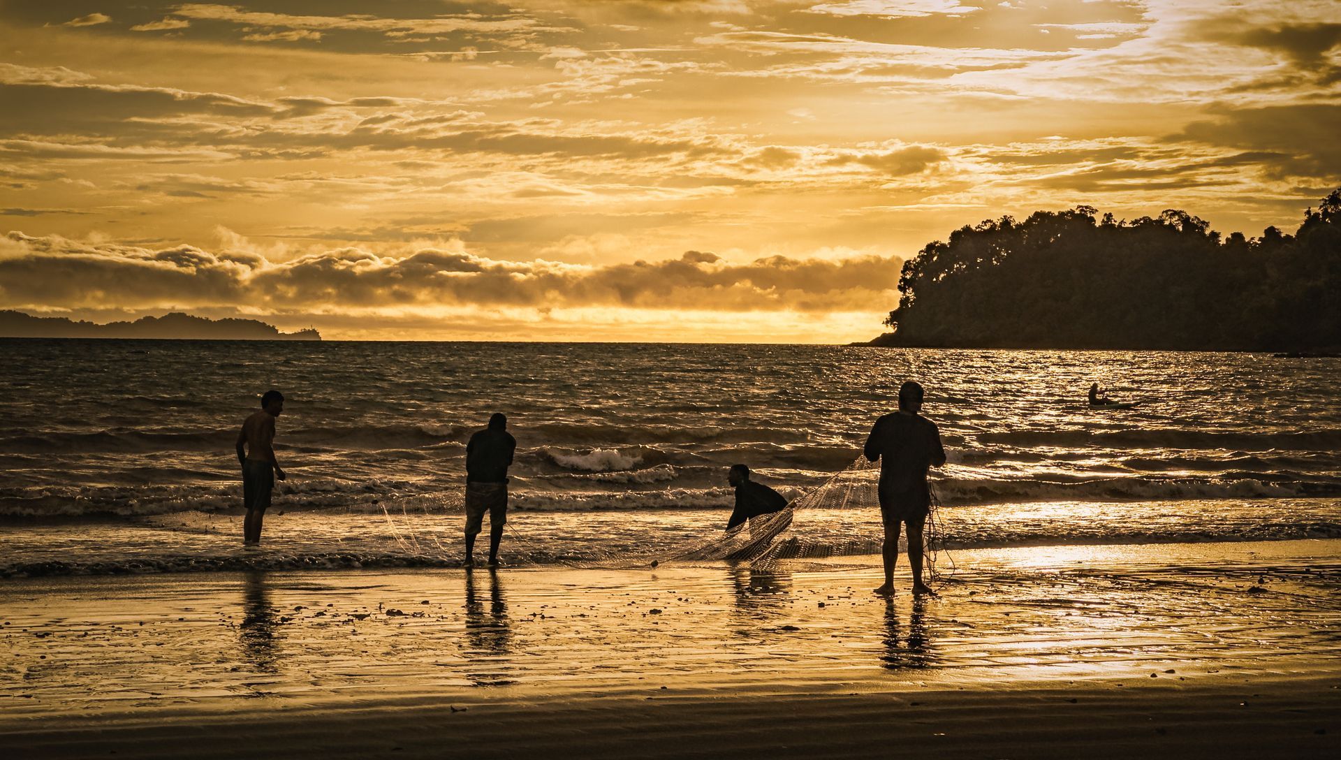 A group of people are standing on a beach at sunset.