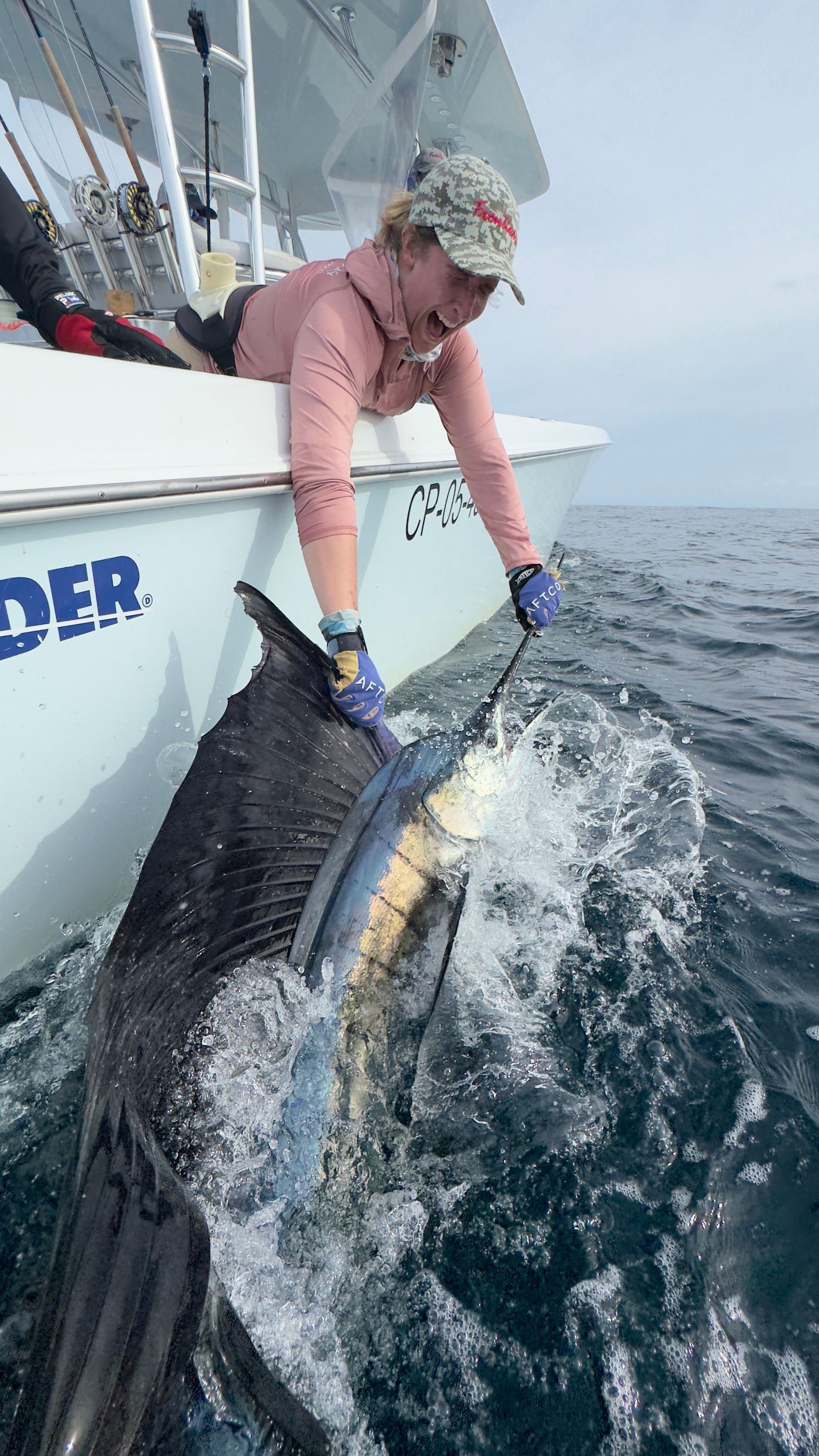 A woman is holding a large fish on a boat in the ocean.