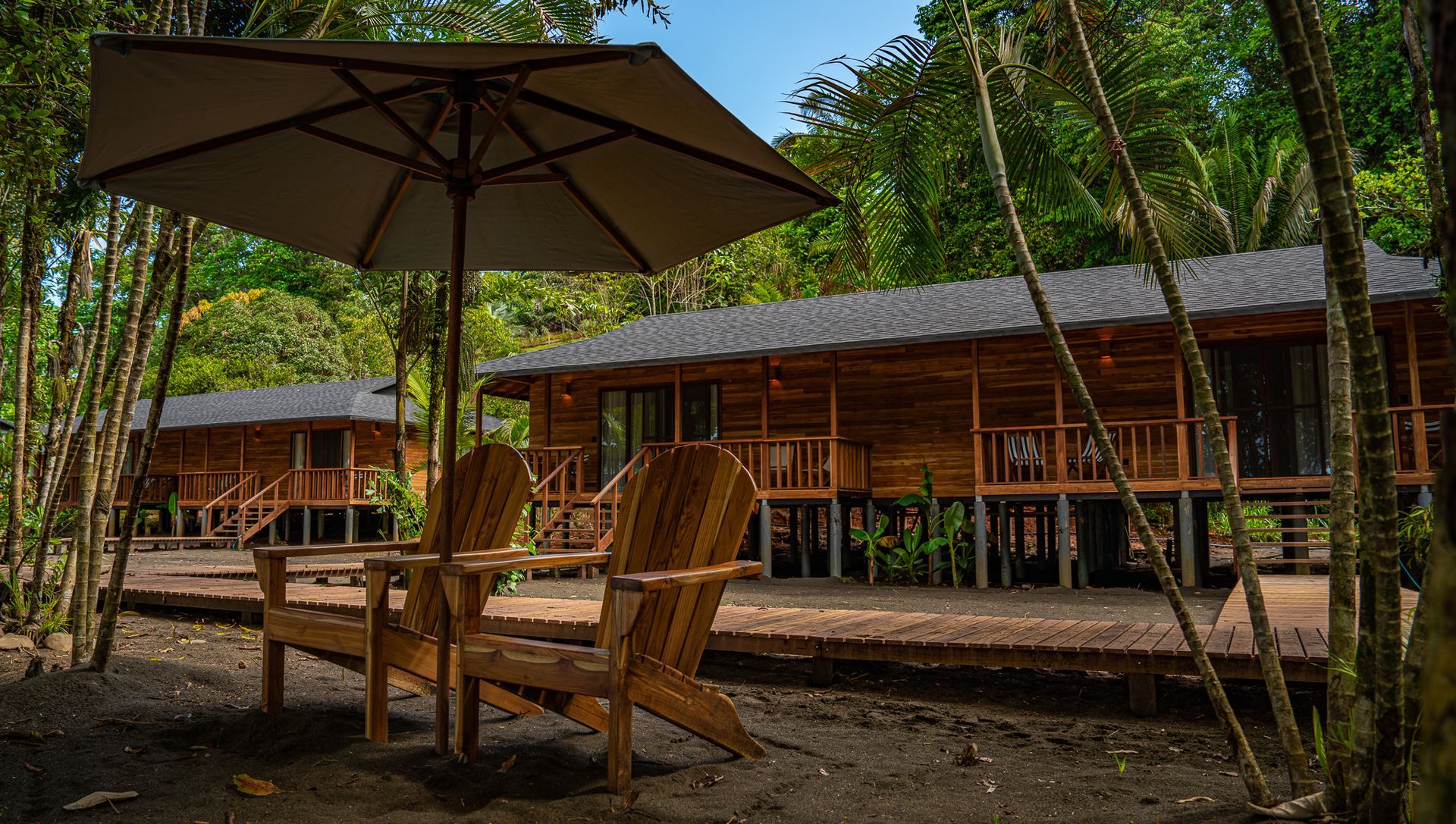 Two wooden chairs under an umbrella in front of a wooden house.
