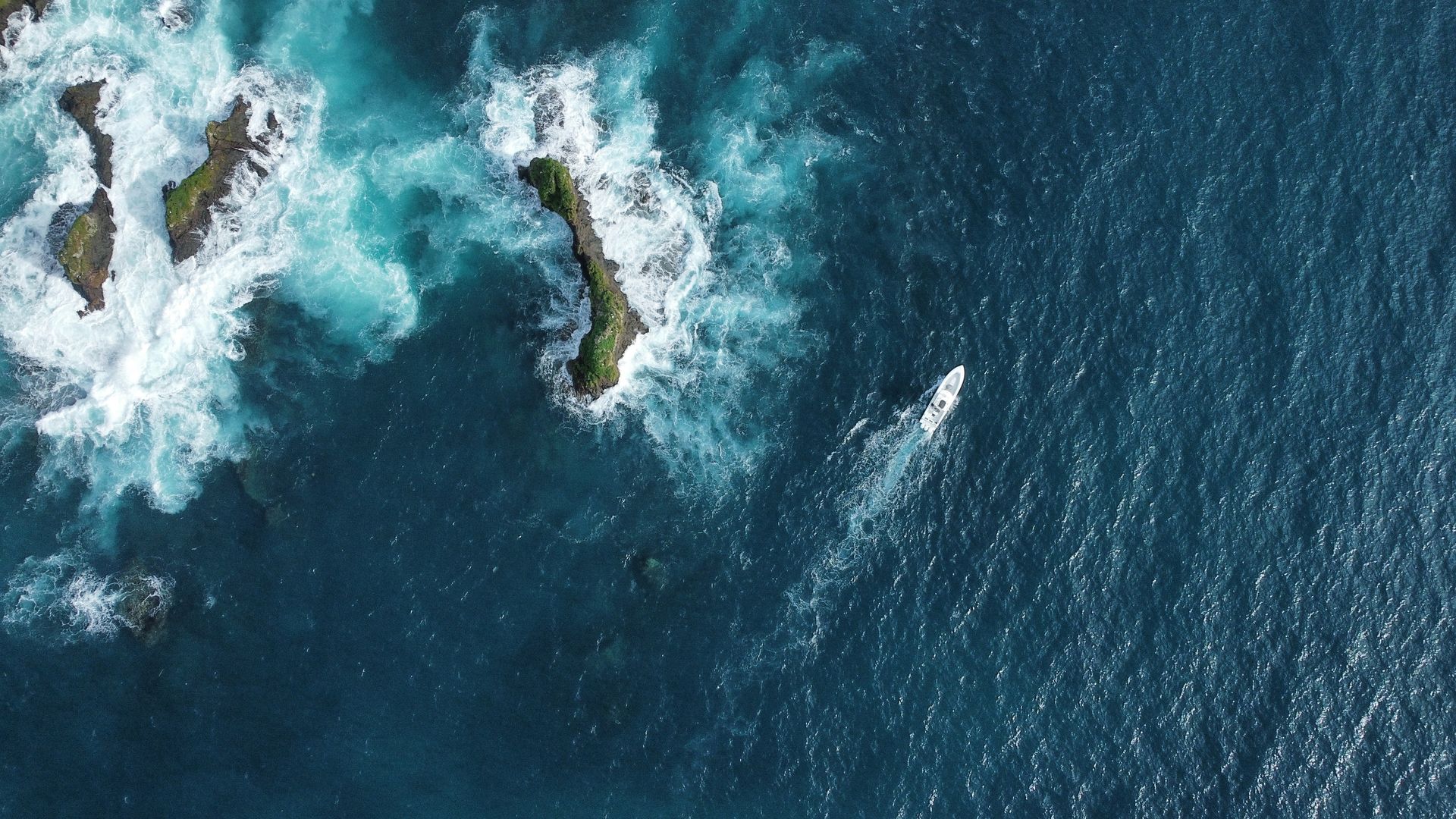 An aerial view of a boat in the ocean near a rocky shoreline.