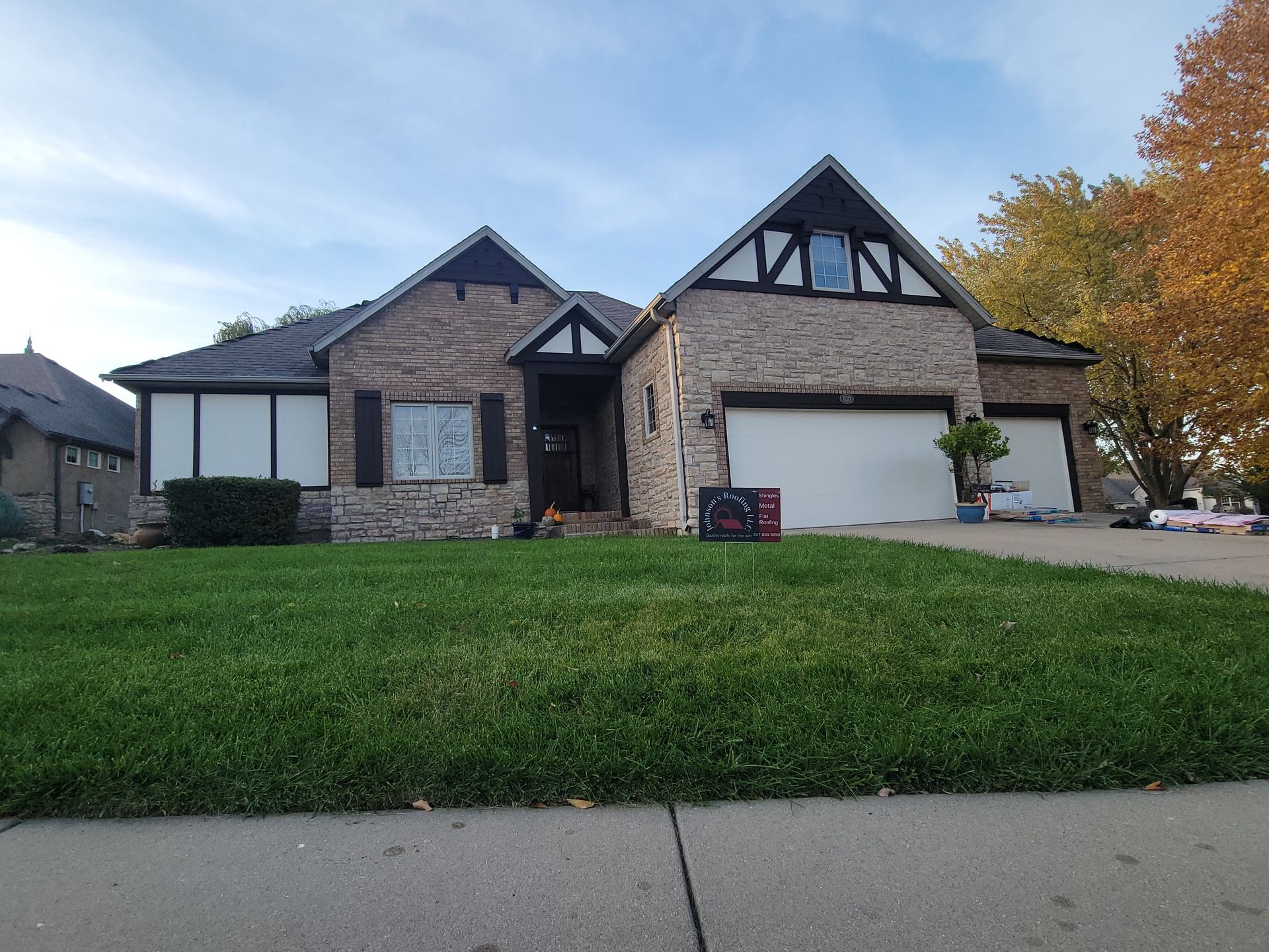 Brick house with lawn and two-car garage under a blue sky, trimmed with dark brown and white accents.