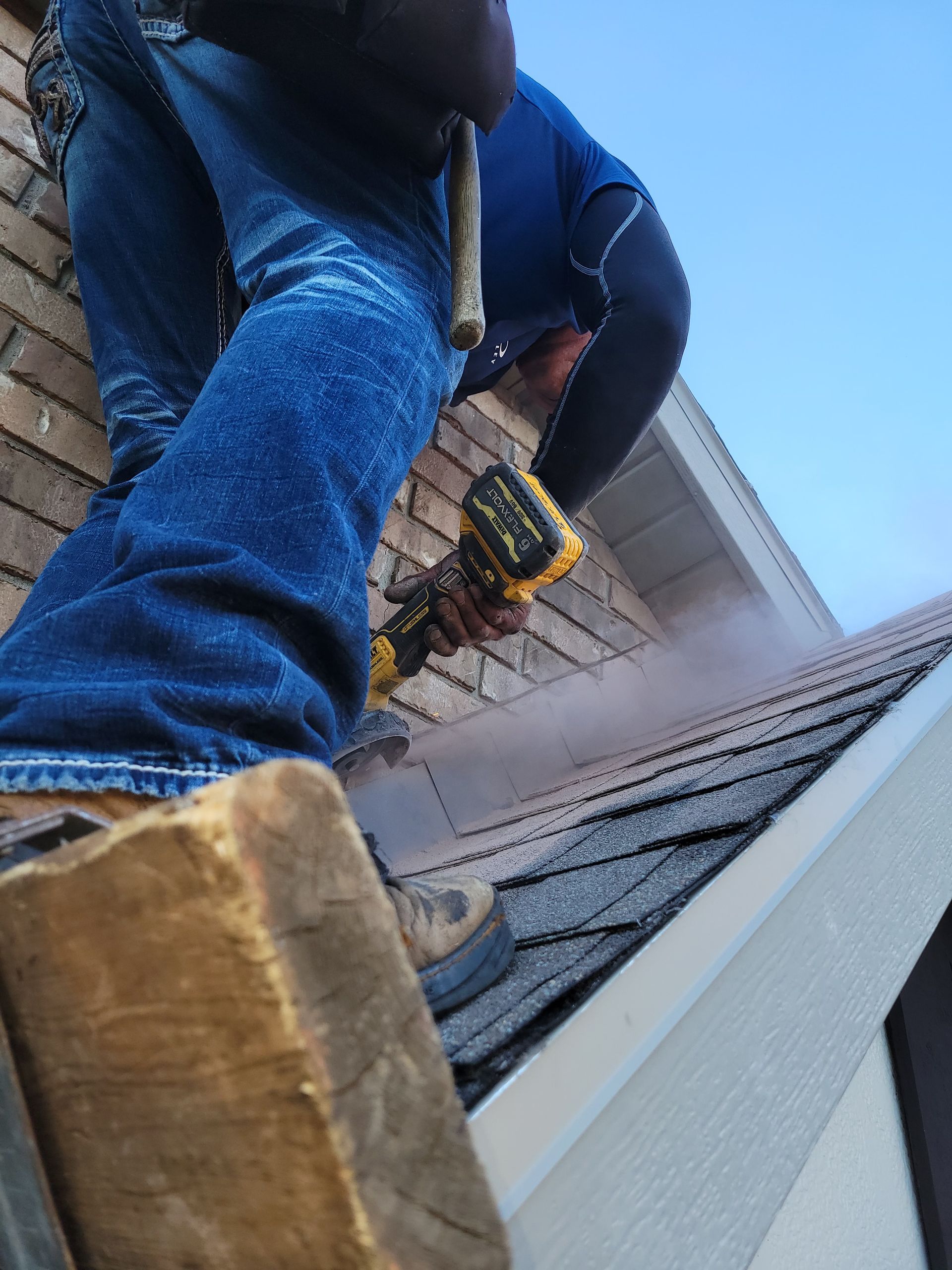 Person on roof uses tool, creating steam. Blue jeans, brown boots, white trim.