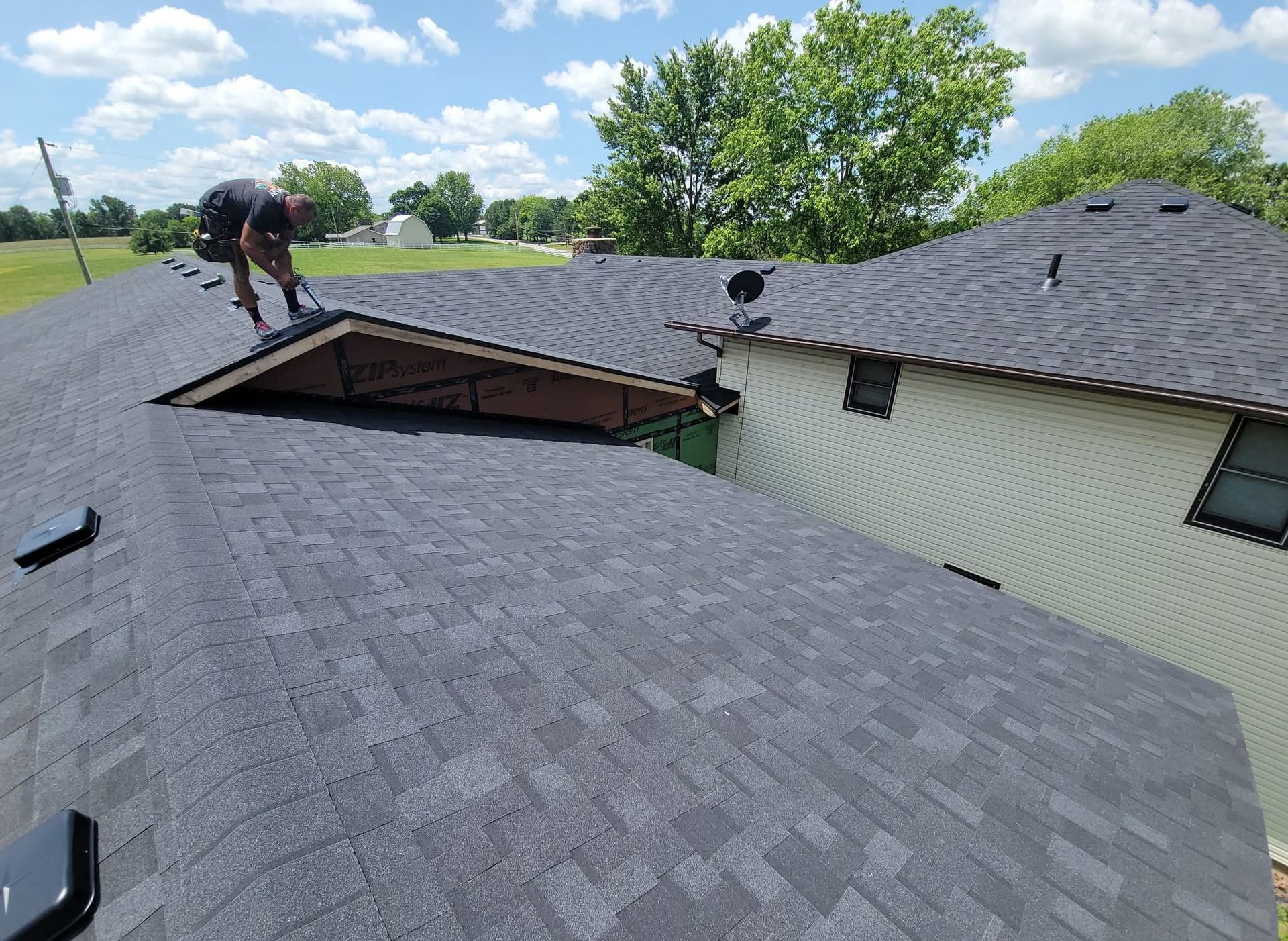 Roofer on a house roof installing shingles; sunny day, blue sky.