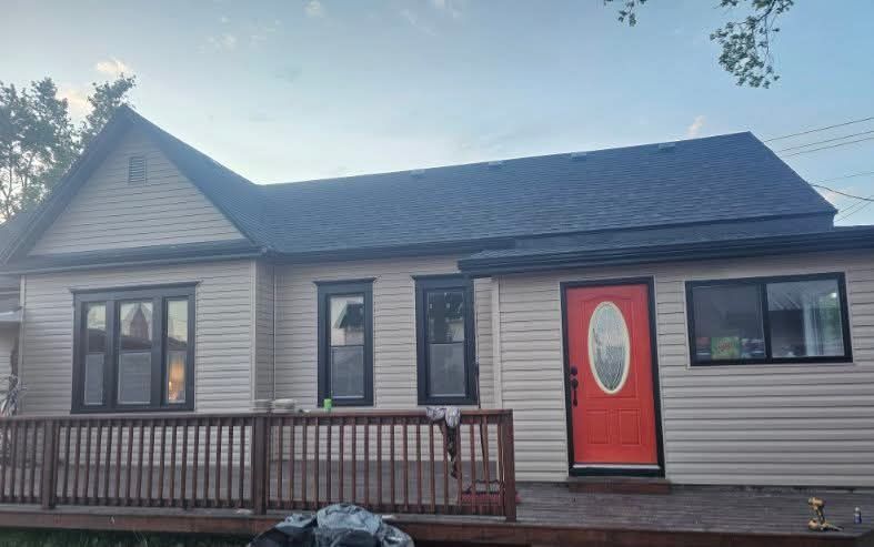 Tan house with black trim, a red door, and a wooden deck. Dark blue sky.