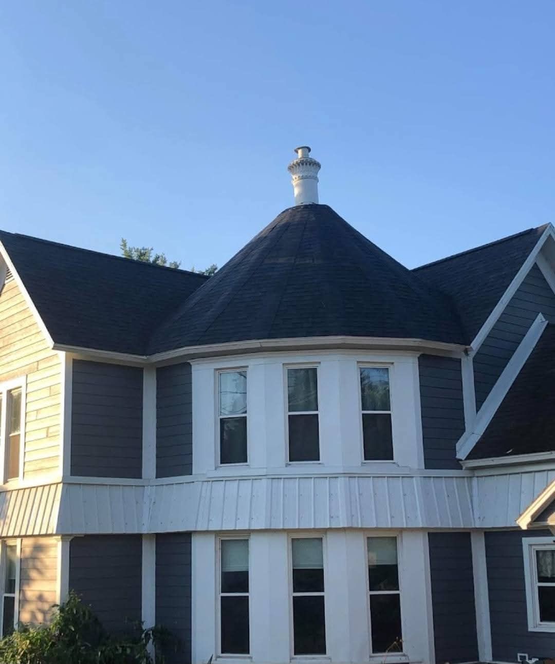 Two-story house with dark roof and blue-gray siding, white trim, and a cylindrical chimney.